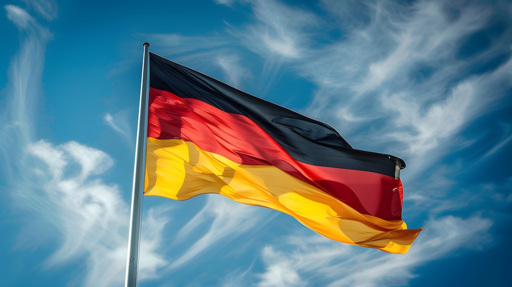 Eine deutsche Flagge weht im Wind vor einem leicht bewölkten Himmel – Deutsch lernen mit Spaß.