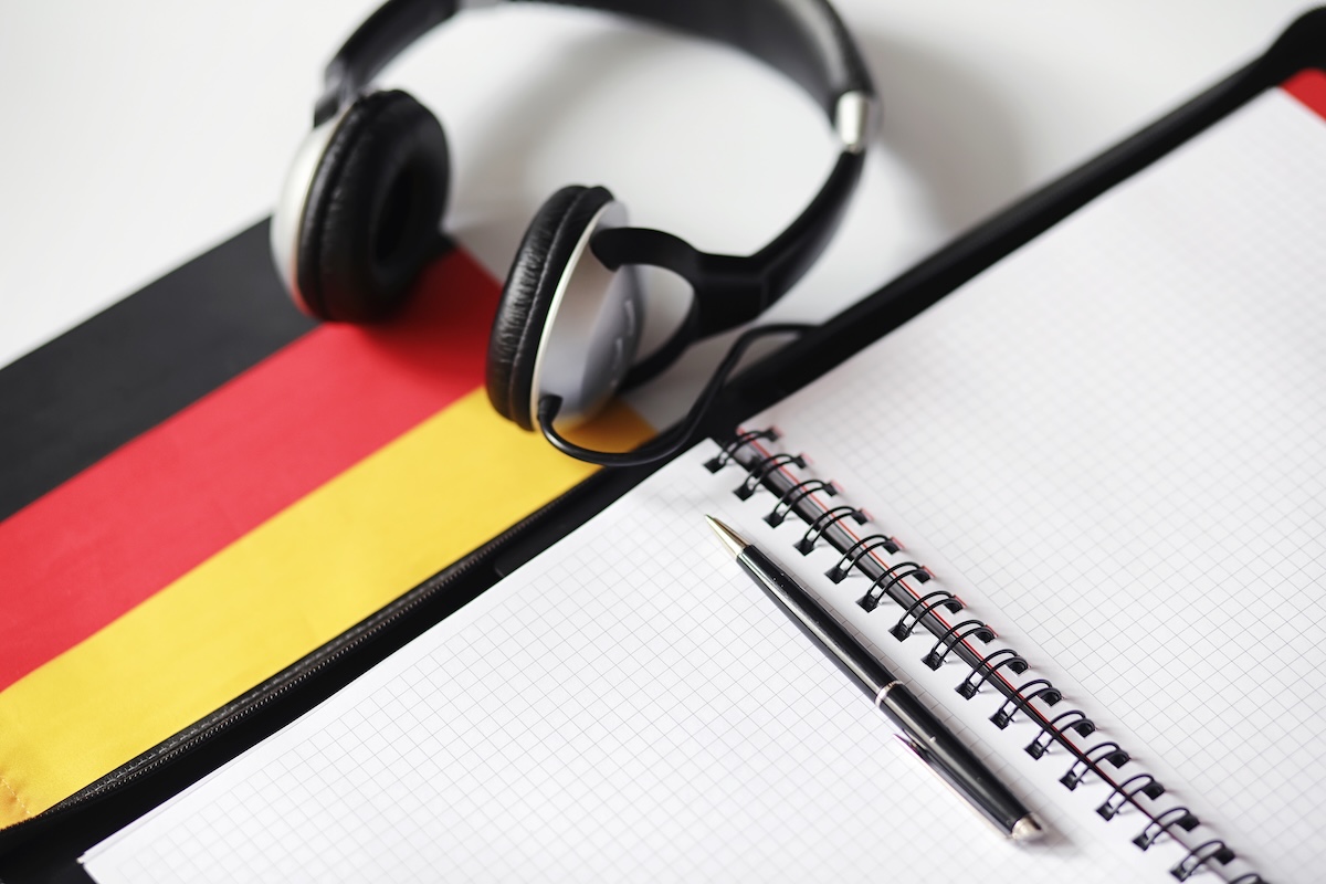 Ein Notizblock mit Stift wartet auf Einträge neuer Vokabeln, Deutschlflagge liegt auf dem Tisch und ein Kopfhörer.